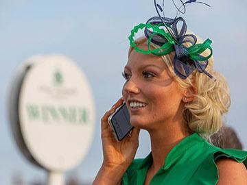 A dressed up woman talking on the phone while at Great Yarmouth Racecourse.