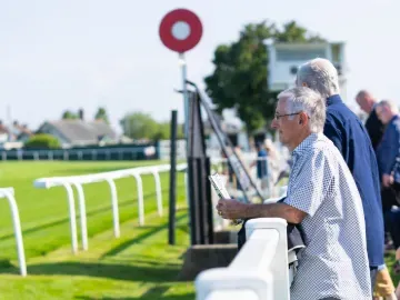 A race goer holding a race card looks out over the track at Great Yarmouth