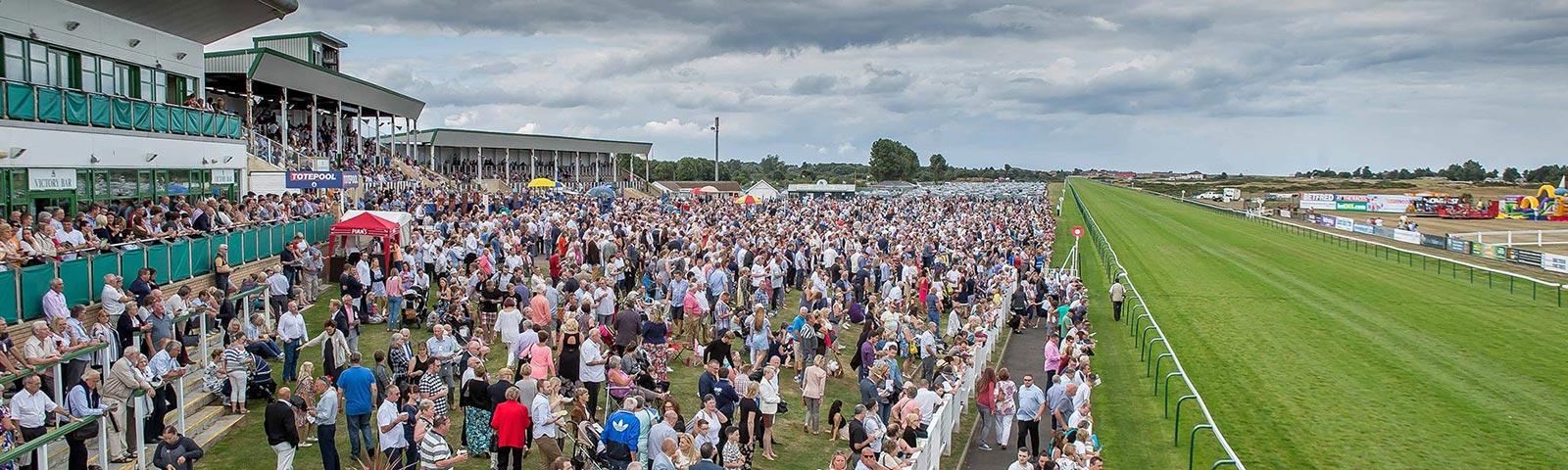 a large crowd of people gather at a racecourse