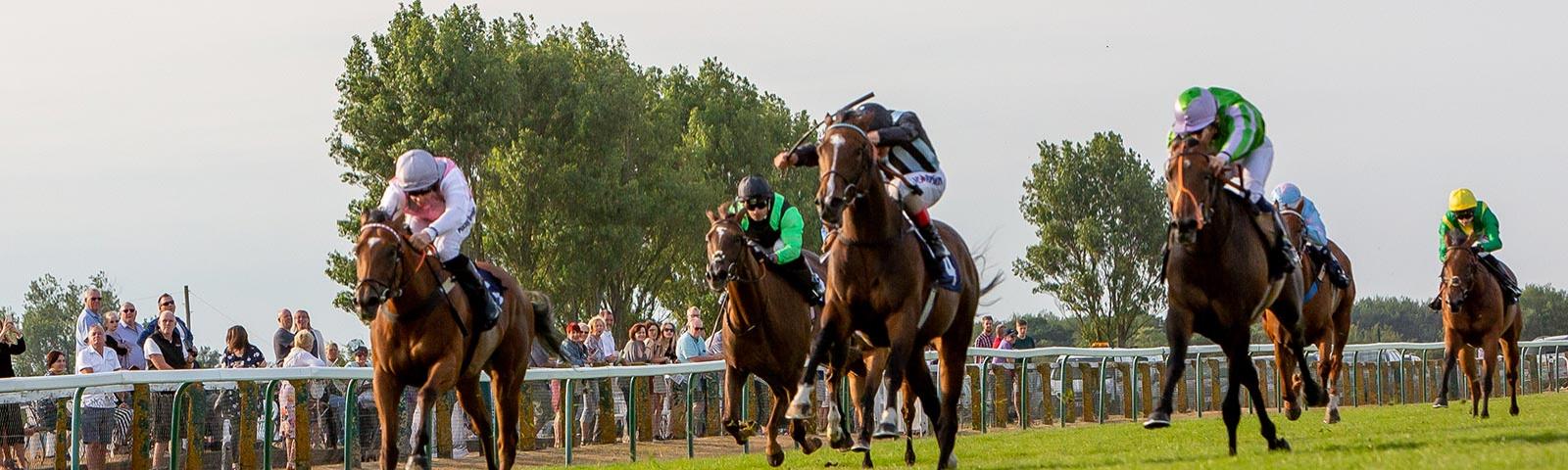 Jockeys racing past crowd of racegoers standing next to the track at Great Yarmouth Racecourse.